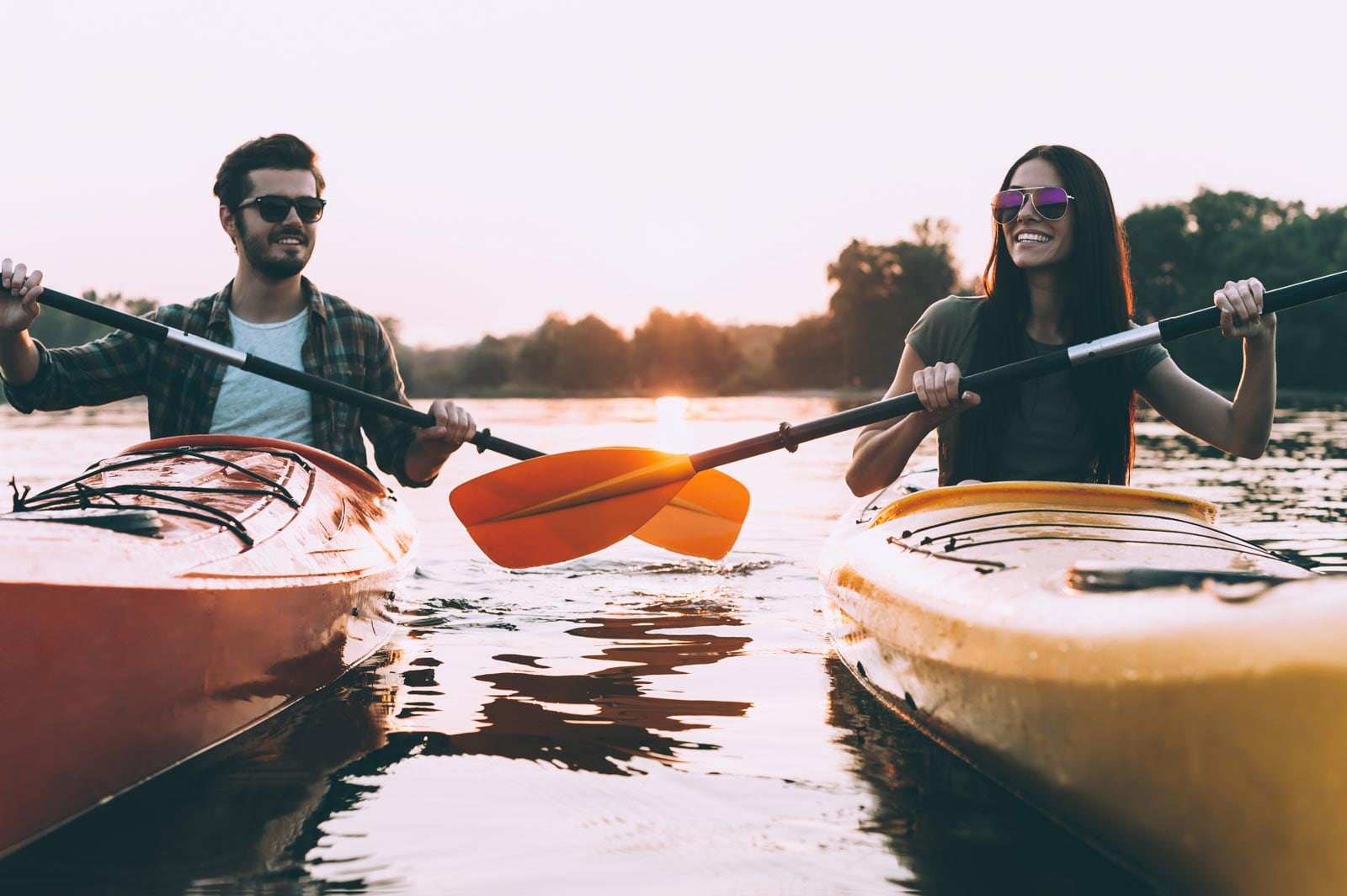 Two people kayaking on a lake at sunset.