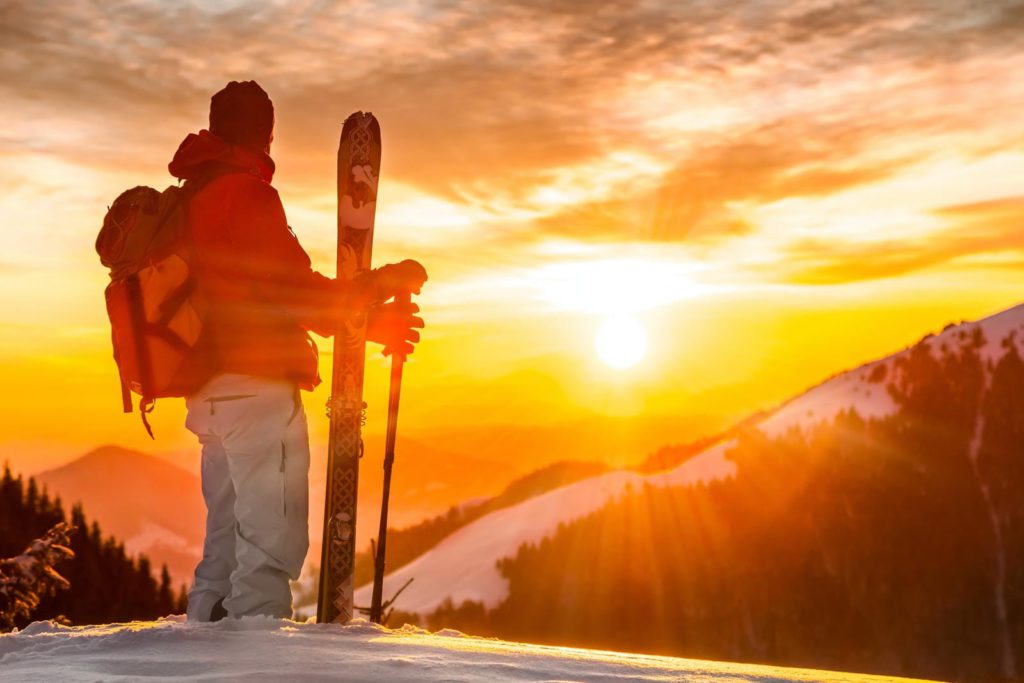 A skier standing on top of a mountain at sunset.
