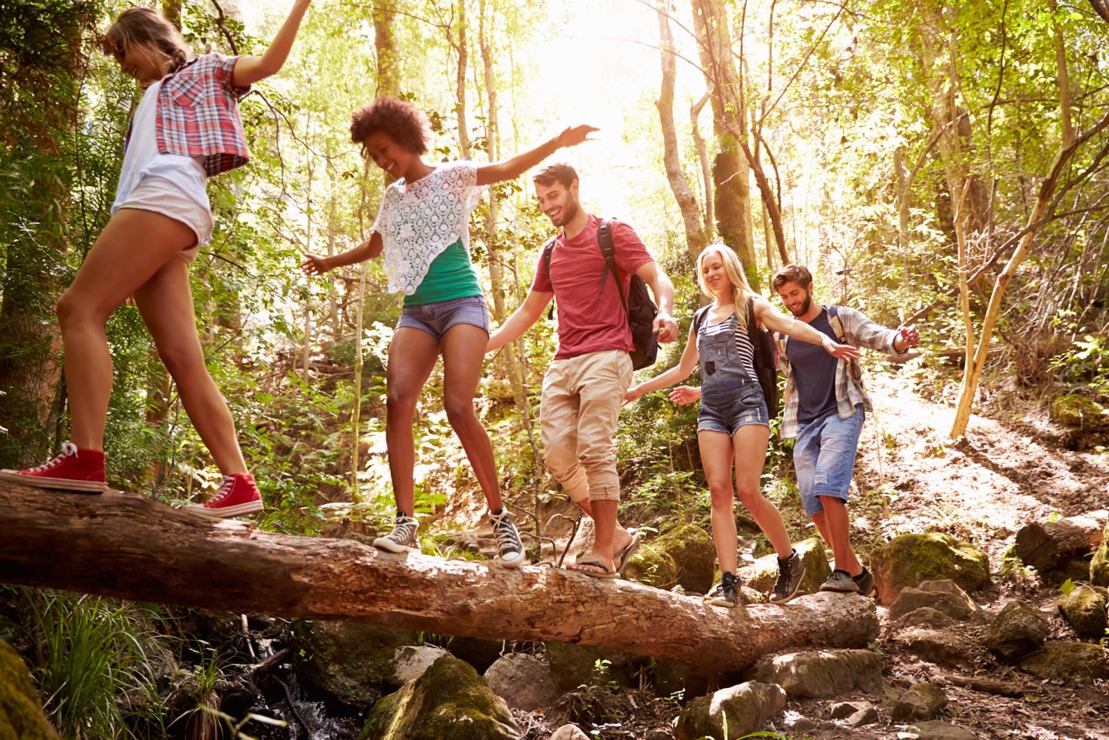 A group of people walking across a log in the woods.
